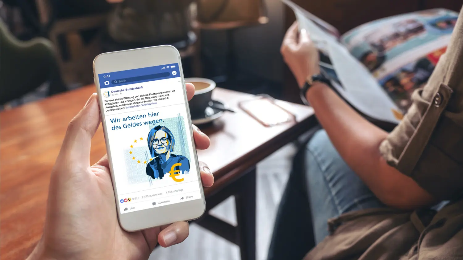 Smartphone mit einem Social-Media-Beitrag der Bundesbank in entspannter Café-Atmosphäre